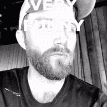 a black and white photo of a man with a beard wearing a hat and a black shirt .