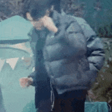 a man in a black jacket is talking on a cell phone while standing in front of a tent .