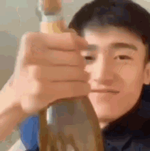 a young man is holding a bottle of beer in his hand and looking at the camera .