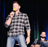 a man in a plaid shirt is holding a microphone on a stage