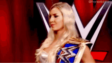 a woman is holding a wrestling championship belt and standing in front of a red curtain .