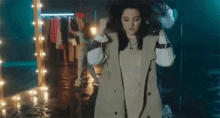 a woman in a trench coat is standing in front of a mirror in a dark room .