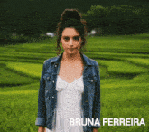 a woman in a white dress and a denim jacket is standing in a field with the name bruna ferreira below her