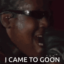 a man wearing sunglasses is singing into a microphone with the words i came to goon below him