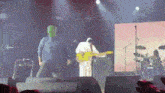a man wearing a green mask is playing a guitar on a stage