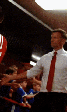 a man in a white shirt and red tie shakes hands with a basketball player in a red and white jersey