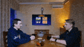 two men are sitting at a table in front of a screen that says ' ambushbox ' on it