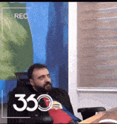 a man with a beard sits in a chair in front of a screen that says rec 360