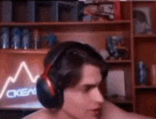 a shirtless man wearing headphones is sitting in front of a bookshelf in a room .