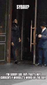 a man in a suit and hat is standing in a doorway talking to another man .