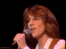 a woman with glasses is singing into a microphone on a stage .