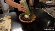 a person is pouring green sauce on a pizza with the words made in animotica below