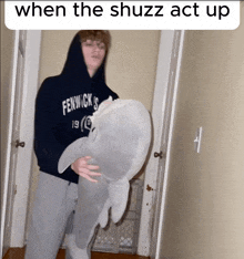 a man in a fenwick sweatshirt holds a stuffed shark