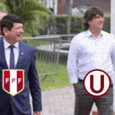 a man in a suit and tie is walking next to another man in a white shirt with the letter u on it