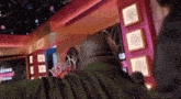 a man in a green jacket stands in front of a pink wall with a sign that says zeus