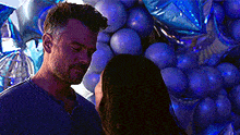 a man and a woman are looking at each other in front of a bunch of blue balloons .