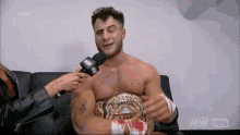 a man is sitting on a couch being interviewed by a woman while wearing a wrestling belt .