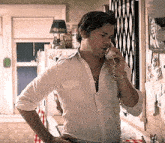 a man in a white shirt is talking on a corded phone in a kitchen .