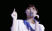 a woman is singing into a microphone and making a heart shape with her finger