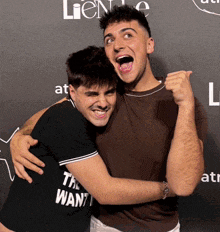 a man wearing a black shirt that says " the want " is hugging another man