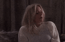 a woman covering her face with her hand while wearing a white sweater
