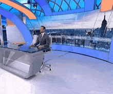 a man sits at a desk in front of a screen that says americas weather now