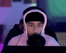 a man wearing headphones and a beanie is sitting in front of a computer monitor .