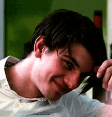 a close up of a man 's face with his hand on his head and a smile on his face .