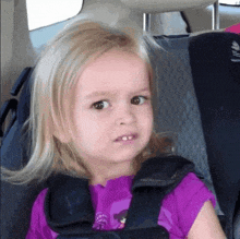 a little girl is sitting in a car seat and making a face