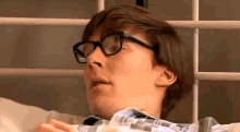 a man wearing glasses and a plaid shirt is laying in bed .