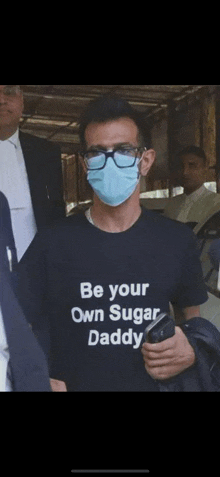 a man wearing a mask and a black t-shirt that says `` be your own sugar daddy '' .