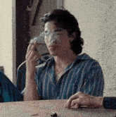 a man in a blue striped shirt is smoking a cigarette while sitting at a table .