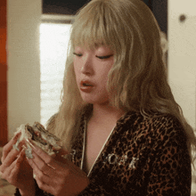 a woman wearing a leopard print jacket holds a sandwich