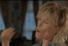 a blonde woman is smoking a cigarette in a room