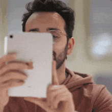 a man with glasses and a beard is looking at his phone