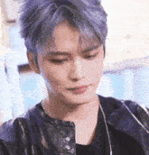 a close up of a man with purple hair wearing a black jacket .