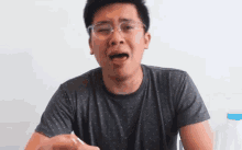 a young man wearing glasses is making a funny face while holding a bottle of water .