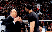 a man in a suit talks to another man in a wrestling ring .
