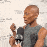 a woman is talking into a microphone in front of a national board of review sign