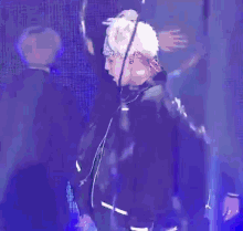 a man with white hair is standing on a stage with a blue background