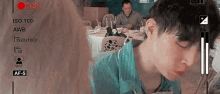 a young boy is sitting at a table eating food while a man watches .