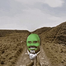 a green m & m standing on a dirt road with a fence in the background