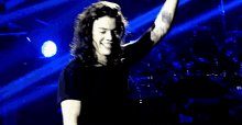 a man with long curly hair is standing on a stage in front of a drum set .