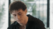 a young man with curly hair is sitting in front of a window looking down .