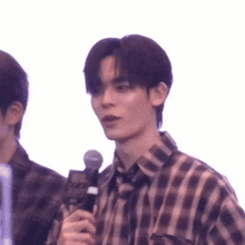 a young man in a plaid shirt is holding a microphone in his hand .