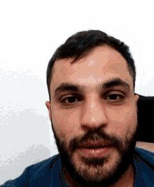 a man with a beard and a blue shirt is looking at the camera .