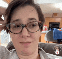 a woman wearing glasses is sitting on a couch in front of a kitchen