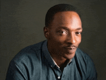 a man in a blue shirt is looking at the camera with a serious look on his face