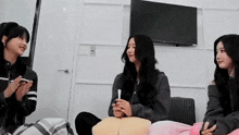three women are sitting on a couch in a room with a television .