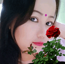a woman with a pink dot on her forehead holds a red rose in her hand